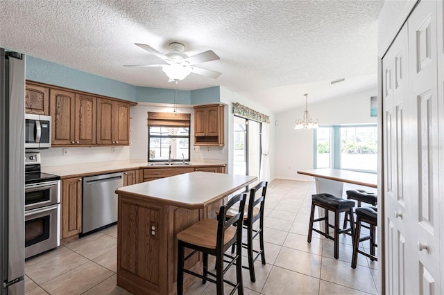 kitchen featuring a center island, a kitchen breakfast bar, light countertops, appliances with stainless steel finishes, and brown cabinets