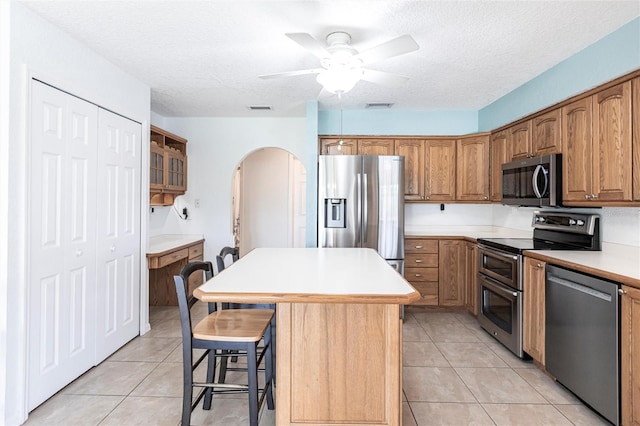 kitchen with stainless steel appliances, a center island, brown cabinetry, and light countertops