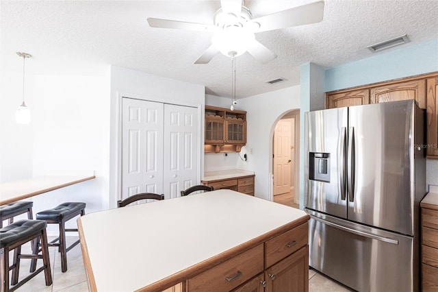 kitchen featuring arched walkways, visible vents, light countertops, brown cabinetry, and stainless steel fridge