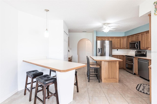 kitchen featuring arched walkways, a breakfast bar, stainless steel appliances, light countertops, and pendant lighting