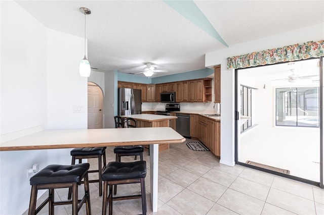 kitchen with stainless steel appliances, light countertops, brown cabinets, open shelves, and decorative light fixtures