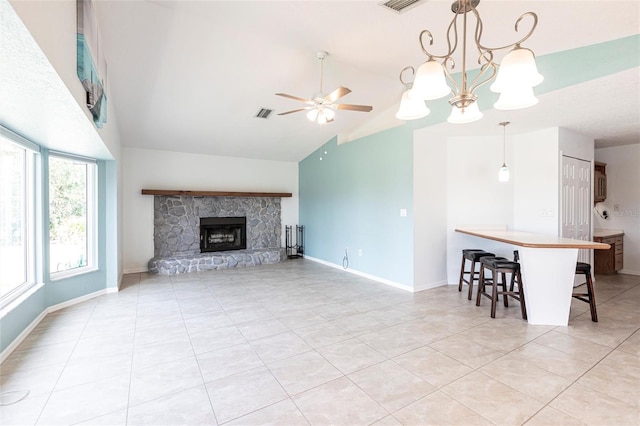 unfurnished living room with light tile patterned floors, a stone fireplace, ceiling fan with notable chandelier, visible vents, and baseboards