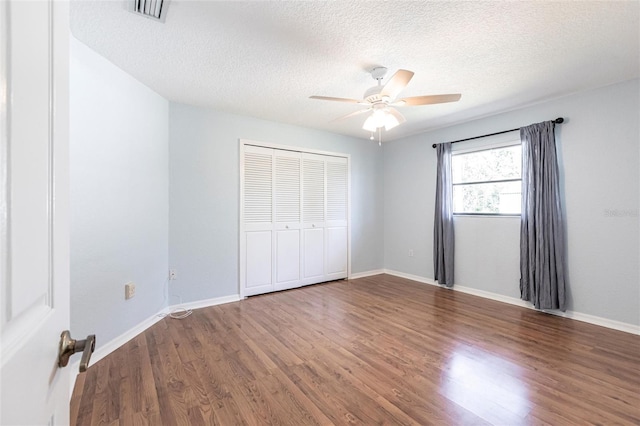 unfurnished bedroom with a closet, visible vents, a textured ceiling, wood finished floors, and baseboards