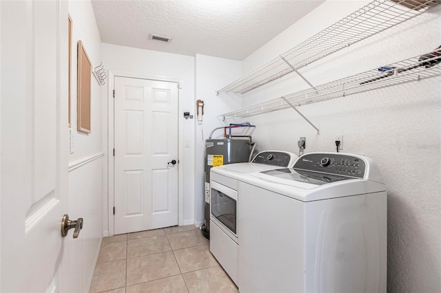 laundry area with light tile patterned floors, water heater, a textured ceiling, laundry area, and independent washer and dryer