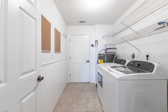 laundry area with a textured ceiling, electric water heater, laundry area, separate washer and dryer, and visible vents