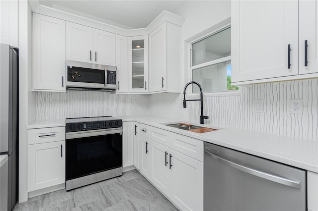 kitchen featuring white cabinets, glass insert cabinets, stainless steel appliances, light countertops, and a sink