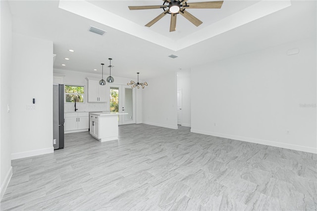 unfurnished living room featuring baseboards, visible vents, a tray ceiling, ceiling fan with notable chandelier, and recessed lighting