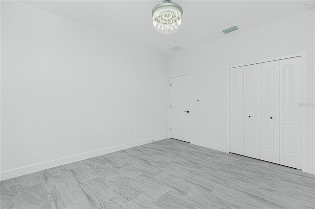 unfurnished bedroom featuring a closet, visible vents, a notable chandelier, and baseboards