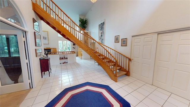 entryway with light tile patterned floors, a fireplace, stairs, and a towering ceiling