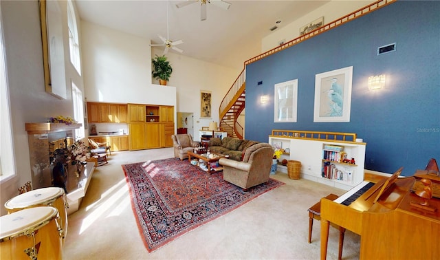 living area with visible vents, light colored carpet, stairway, a towering ceiling, and ceiling fan