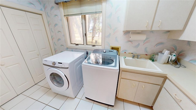 clothes washing area with light tile patterned flooring, a sink, washer and dryer, cabinet space, and wallpapered walls