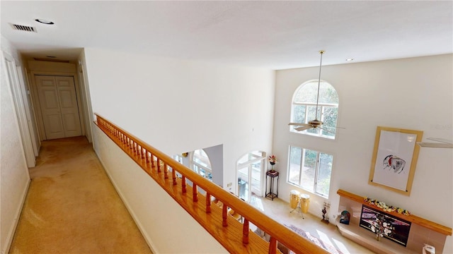 hallway featuring stairs, a towering ceiling, visible vents, and light colored carpet