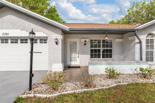 entrance to property featuring ceiling fan, a shingled roof, an attached garage, and stucco siding