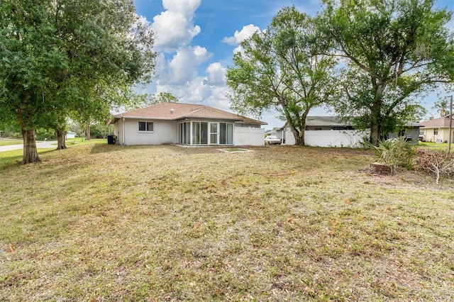 rear view of house featuring stucco siding, fence, a lawn, and a sunroom