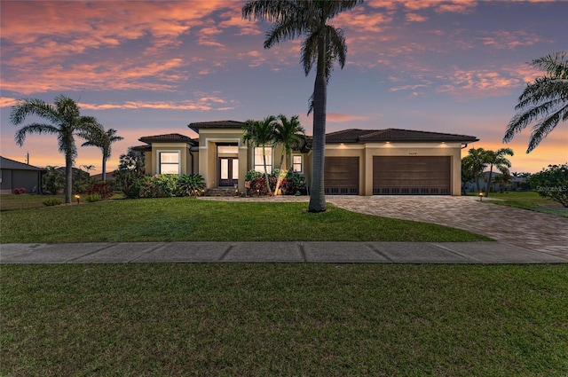 view of front of property with decorative driveway, stucco siding, a garage, a tiled roof, and a front lawn