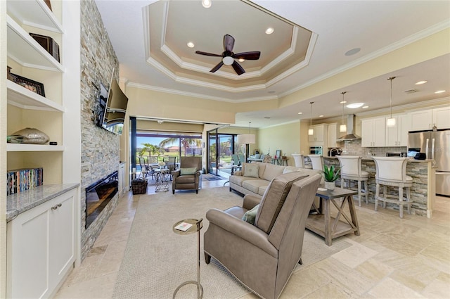 living room featuring ceiling fan, a fireplace, visible vents, a raised ceiling, and crown molding