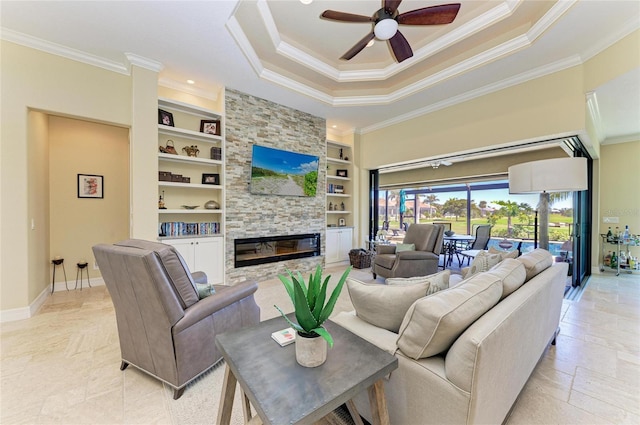 living room with baseboards, built in features, a tray ceiling, crown molding, and a fireplace