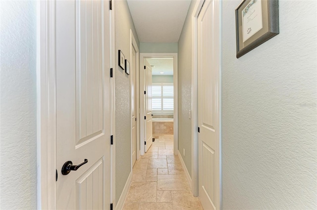 hallway with a textured wall, stone tile flooring, and baseboards