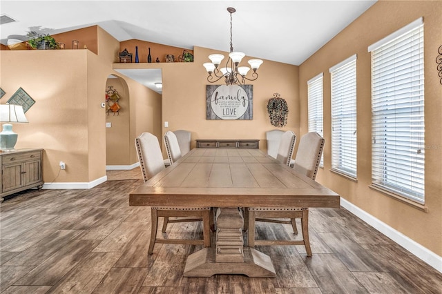 dining room featuring a healthy amount of sunlight, vaulted ceiling, a notable chandelier, and wood finished floors