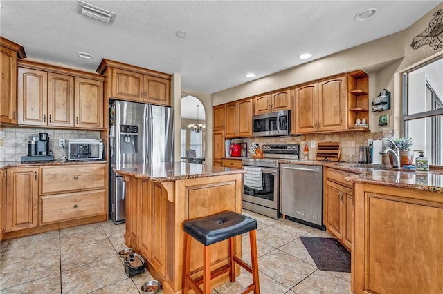 kitchen with arched walkways, stainless steel appliances, a center island, open shelves, and a kitchen bar