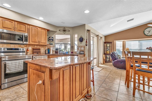 kitchen featuring lofted ceiling, light stone counters, stainless steel appliances, a kitchen island, and visible vents