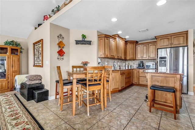 kitchen featuring brown cabinetry, stainless steel fridge with ice dispenser, open floor plan, a kitchen bar, and backsplash