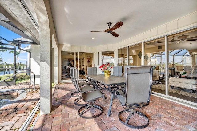 view of patio with a lanai, a water view, ceiling fan, and outdoor dining space