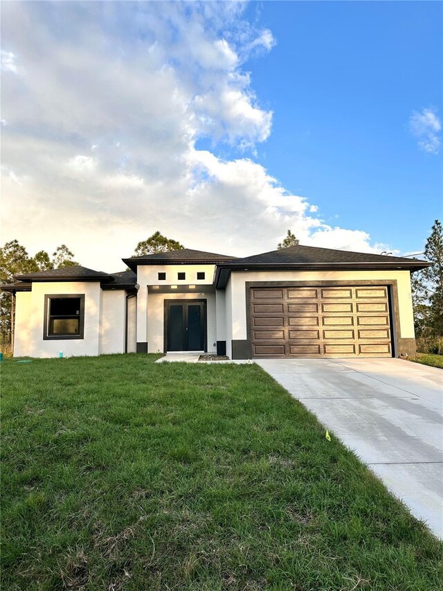 prairie-style home with an attached garage, driveway, french doors, stucco siding, and a front lawn