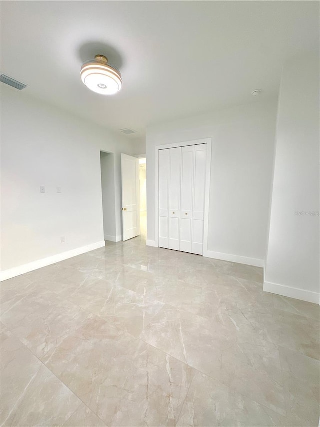 unfurnished bedroom featuring marble finish floor, visible vents, baseboards, and a closet