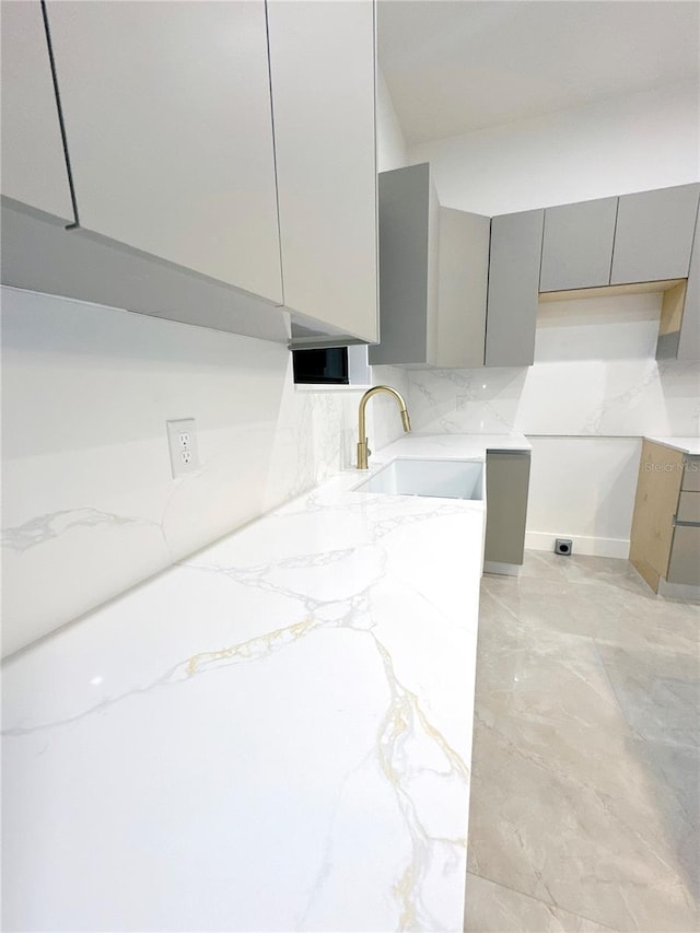 kitchen featuring light stone counters, modern cabinets, a sink, and gray cabinetry