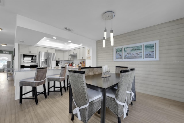 dining room featuring light wood-style flooring, a raised ceiling, visible vents, and recessed lighting