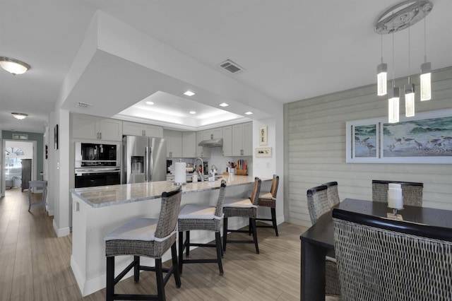 kitchen featuring visible vents, a raised ceiling, a peninsula, stainless steel appliances, and a kitchen bar