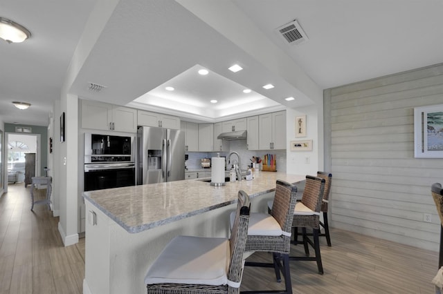 kitchen with visible vents, appliances with stainless steel finishes, a breakfast bar, a peninsula, and a tray ceiling