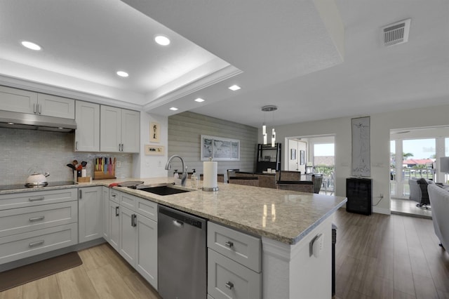 kitchen featuring black electric stovetop, under cabinet range hood, a peninsula, stainless steel dishwasher, and a tray ceiling