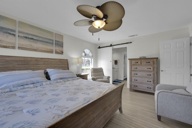 bedroom featuring ceiling fan, a barn door, connected bathroom, visible vents, and light wood-type flooring