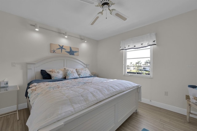 bedroom with a ceiling fan, rail lighting, baseboards, and wood finished floors