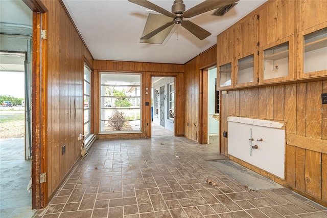 interior space featuring ceiling fan, wood walls, brick floor, and visible vents