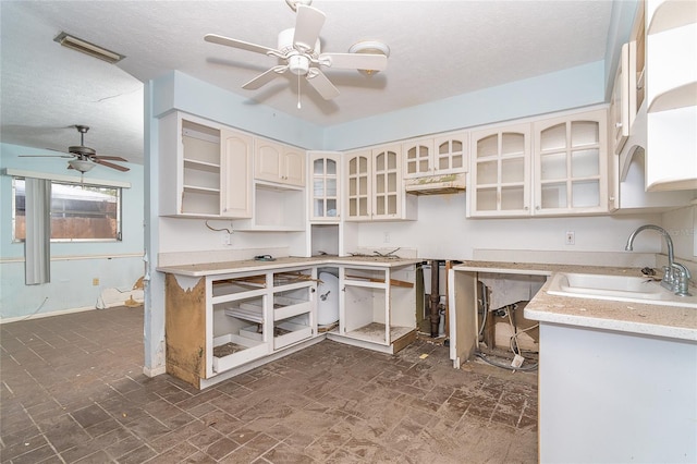 kitchen featuring ceiling fan, a sink, light countertops, open shelves, and glass insert cabinets