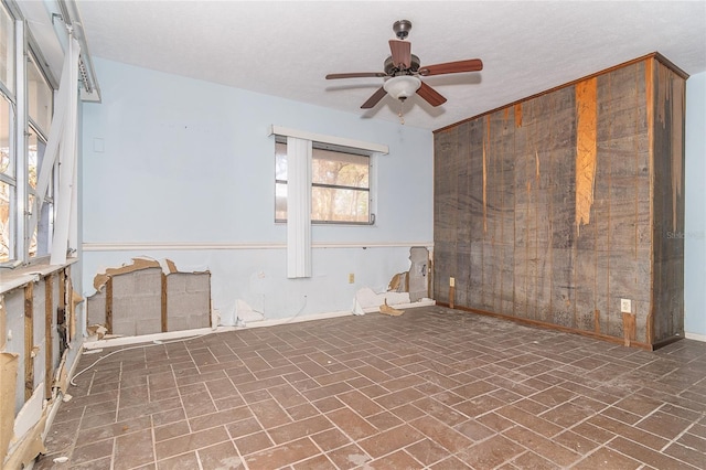 empty room featuring ceiling fan, brick floor, and baseboards