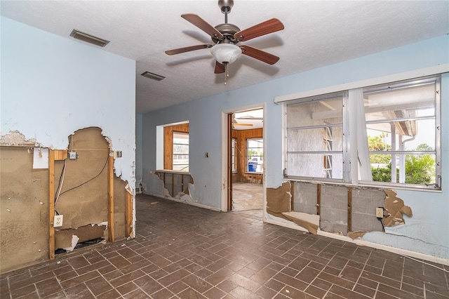 unfurnished room with brick floor, a textured ceiling, visible vents, and a ceiling fan