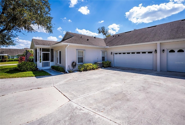 single story home featuring an attached garage, central air condition unit, concrete driveway, roof with shingles, and stucco siding