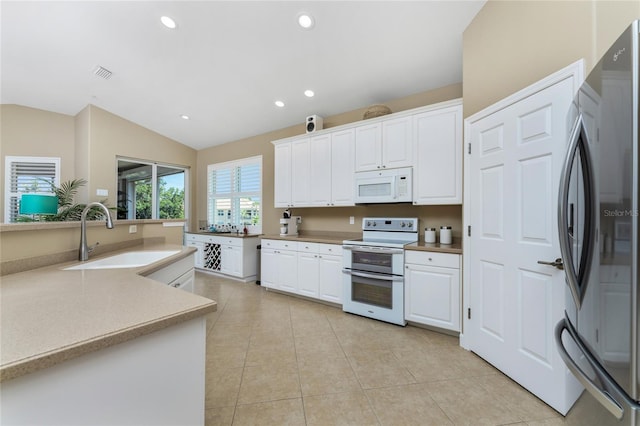 kitchen with white appliances, light tile patterned floors, lofted ceiling, white cabinetry, and a sink