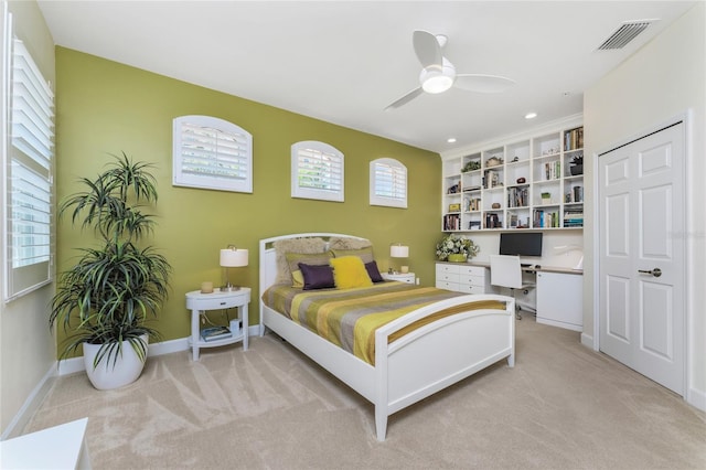 bedroom with light colored carpet, a ceiling fan, baseboards, visible vents, and built in desk