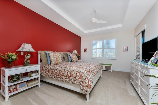 bedroom with light carpet, a tray ceiling, a ceiling fan, and baseboards