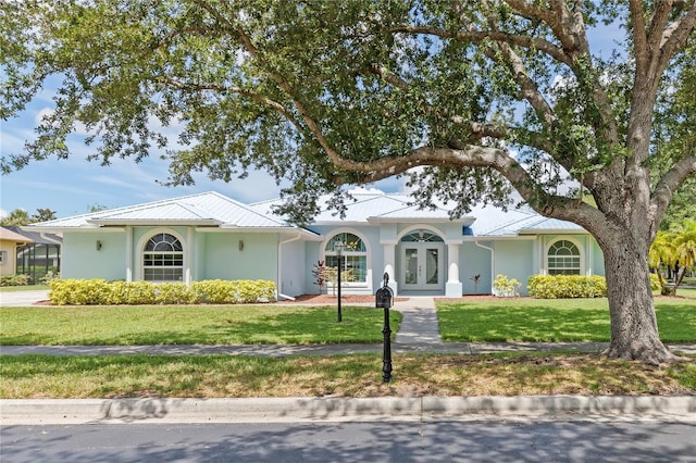 view of front facade with metal roof, french doors, a front lawn, and stucco siding