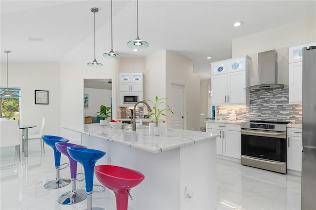 kitchen with pendant lighting, stainless steel appliances, tasteful backsplash, white cabinets, and wall chimney exhaust hood