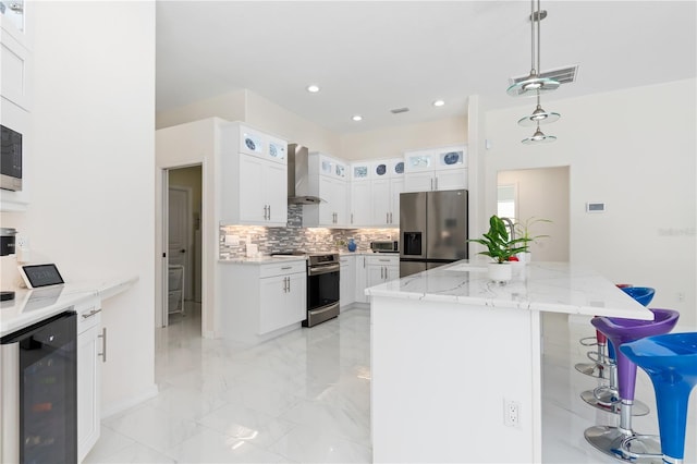 kitchen with pendant lighting, appliances with stainless steel finishes, white cabinets, beverage cooler, and wall chimney exhaust hood