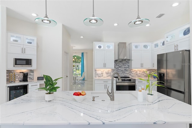 kitchen with wall chimney exhaust hood, appliances with stainless steel finishes, glass insert cabinets, and decorative light fixtures