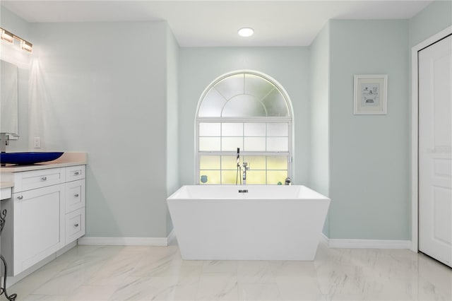 bathroom with marble finish floor, a freestanding tub, vanity, and baseboards