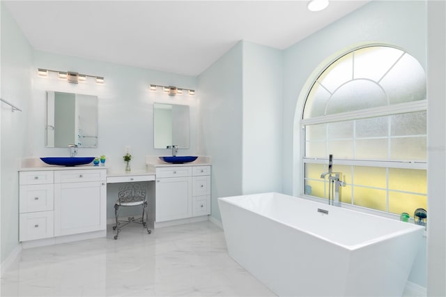 bathroom with a freestanding bath, marble finish floor, two vanities, and a sink